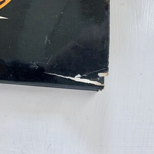 May include: A black hardcover book with a white star and orange design on the front cover. The book has a tear on the top right corner of the cover.