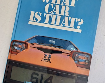 May include: A blue book with the title "What Car Is That?" on the cover. The cover features a close-up of an orange car with a license plate that reads "614". The book is a comprehensive guide to cars of the world by Peter Roberts.