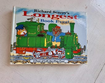May include: A hardcover children's book titled Richard Scarry's Longest Book Ever! featuring a green steam locomotive with a cat in a blue cap and a brown creature on the engine. The cover includes the text 8 Feet of Lift-the-Flap Fun!.