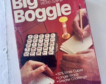 May include: A red box game called "Big Boggle" by Parker Brothers. The box shows a close-up of the game board with letter cubes and a person writing down words on a notepad. The text on the box says "50% More Cubes, Longer Words, Greater Challenge".