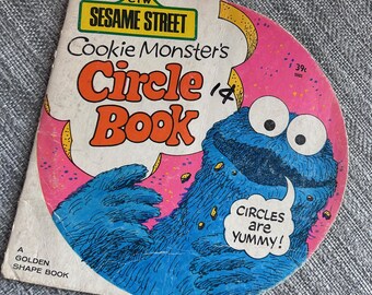 May include: Vintage Sesame Street "Cookie Monster's Circle Book" with a blue Cookie Monster illustration. The cover features the text "Circles are Yummy!" and the book is a Golden Shape Book.