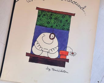 May include: A softcover book titled A Ziggy Book Especially For You: When you're not around... by Tom Wilson. The cover features a cartoon character with a large nose resting on a windowsill, a green patterned shade, and a small orange flower pot.