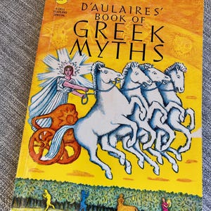 以下が含まれることがあります： 黄色い表紙のペーパーバック「D'Aulaires' Book of Greek Myths」。表紙には、4頭の白い馬に引かれた戦車に乗る人物が描かれており、下部には小さな人物やケンタウロスが風景の中に配置されています。