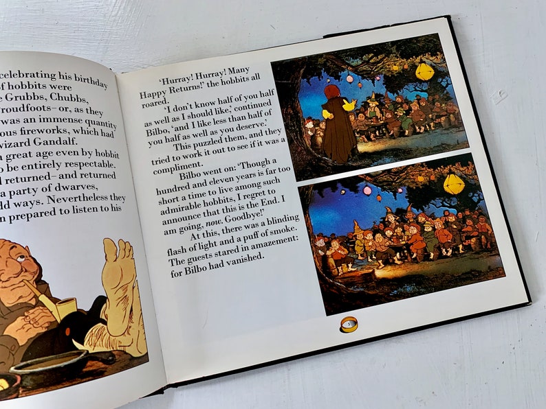 May include: A book open to a page with illustrations of hobbits celebrating a birthday party. The text on the page reads, "Hurray! Hurray! Many Happy Returns!" and "I don't know half of you half as well as I should like, continued Bilbo, 'and I like less than half of you half as well as you deserve."