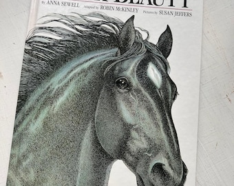 May include: A hardcover book titled Black Beauty by Anna Sewell, adapted by Robin McKinley with illustrations by Susan Jeffers. The white cover features a detailed black and white ink drawing of a horse head with a white star on its forehead.