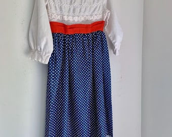 May include: A white dress with a lace bodice and a blue polka dot skirt. The dress has a red ribbon around the waist.