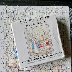 May include: A Beatrix Potter jigsaw puzzle featuring Peter Rabbit and Benjamin Bunny. The puzzle box shows an illustration of the characters in a garden setting. The assembled size is 7.5 inches by 7.5 inches, with 100 interlocking pieces.