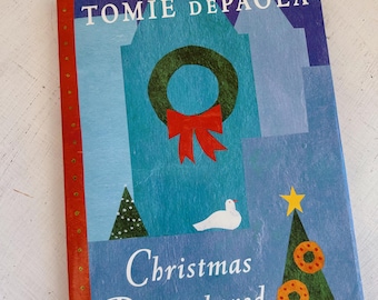 May include: A hardcover book titled "Christmas Remembered" by Tomie dePaola. The cover features a teal background with a green wreath and red bow, a white dove, and a Christmas tree decorated with ornaments. The spine is red with gold dots.