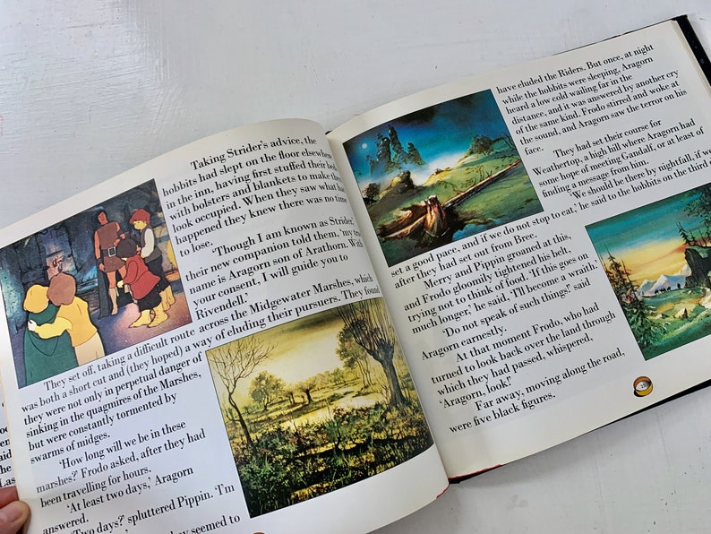 May include: An open book with illustrations of a forest and a group of people. The text on the page reads "Taking Strider's advice, the hobbits had slept on the floor..." and "They set off, taking a difficult route across the Midgewater Marshes..."