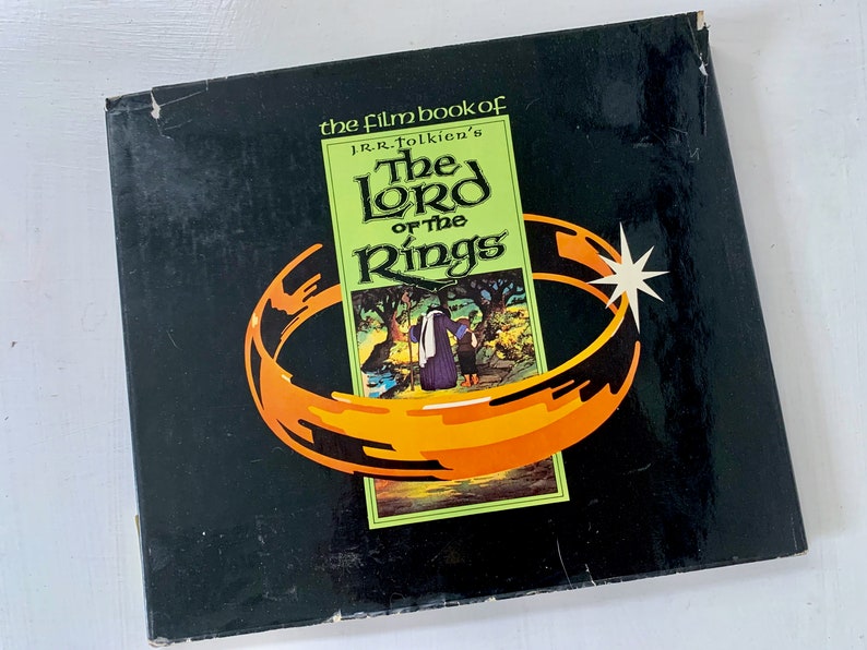 May include: A black box with a gold ring and a green and white image of a scene from "The Lord of the Rings" movie. The box has the text "the film book of J.R.R. Tolkien's The Lord of the Rings" on the front.