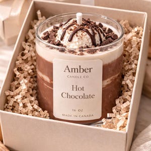 Hot chocolate candle in a clear glass jar designed to look like a warm cup of cocoa, topped with realistic whipped cream wax and chocolate drizzle, handmade soy candle from Amber Candle Co.