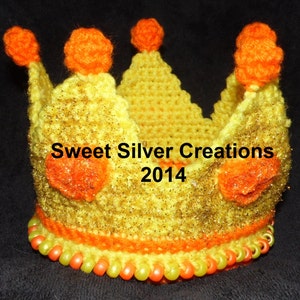 Könnte beinhalten: Eine gelbe gehäkelte Krone mit orangefarbenen Bommeln und Perlen. Die Krone hat ein glitzerndes Finish und der Text "Sweet Silver Creations 2014" ist sichtbar.