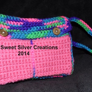 Könnte beinhalten: Eine rosafarbene gehäkelte Umhängetasche mit einem mehrfarbigen Riemen. Die Tasche hat zwei Fächer und zwei braune Knöpfe. Auf der Vorderseite der Tasche steht "Sweet Silver Creations 2014".