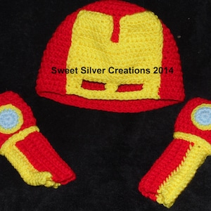 May include: A crocheted Iron Man costume set for a baby, featuring a red and yellow hat with a mask and matching red and yellow arm warmers.