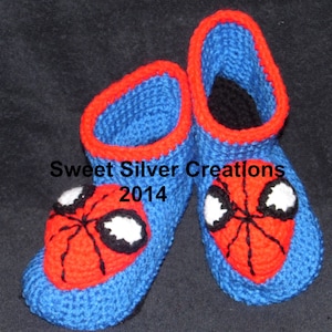 May include: Blue and red crocheted slippers with a Spiderman design. The slippers have a black spider web and white eyes.