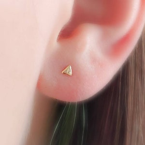 May include: A pair of gold triangle stud earrings. The earrings are small and delicate, and they are perfect for everyday wear.