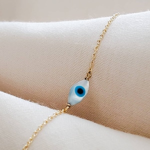 May include: A gold chain bracelet with a blue and white evil eye charm.