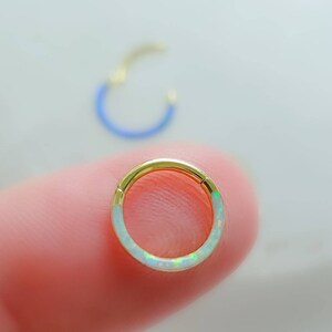 May include: A gold hoop earring with a white opal inlay. The hoop is thin and delicate, and the opal is set in a smooth, rounded shape.