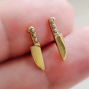 May include: A pair of gold-toned earrings shaped like small kitchen knives.