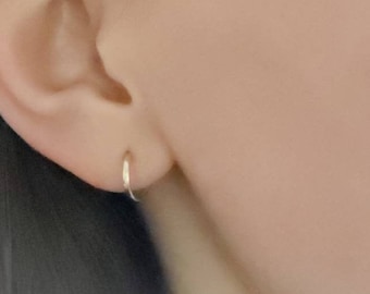 May include: A close-up of a person's ear with a small, silver hoop earring. The earring is simple and understated, and it is a popular choice for everyday wear.