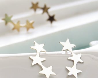 May include: A pair of silver star-shaped earrings. Each earring features five stars connected in a curved line.