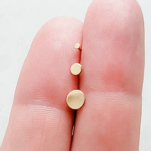 May include: Three gold-colored, round stud earrings of varying sizes are displayed. The largest earring is approximately 0.25 inches in diameter, the middle one is 0.12 inches, and the smallest is 0.06 inches. The earrings are shown against a light background.