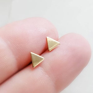 May include: A pair of gold triangle stud earrings. The earrings are small and delicate, and they are perfect for everyday wear.
