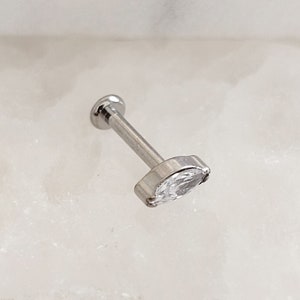 May include: A silver barbell with a clear marquise-shaped gemstone. The barbell is a body piercing jewelry item.