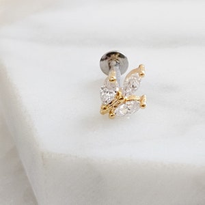 May include: A silver and gold butterfly-shaped body jewelry piece with clear cubic zirconia stones.