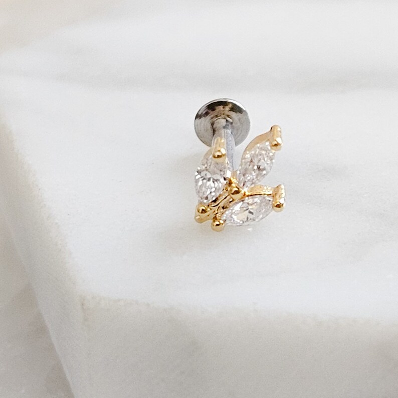 May include: A silver and gold butterfly-shaped body jewelry piece with clear cubic zirconia stones.