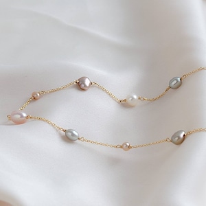 May include: A delicate gold chain necklace featuring a selection of pearl shapes and colours, including white, grey, and pink.