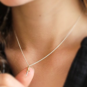 May include: A silver chain necklace with a small gold dagger pendant.