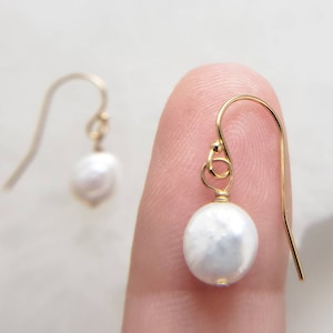 May include: A pair of gold earrings with a white pearl dangling from each. The pearls are round and smooth.