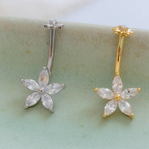May include: Two belly button rings with a flower design. One ring is silver with clear stones and the other is gold with clear stones.