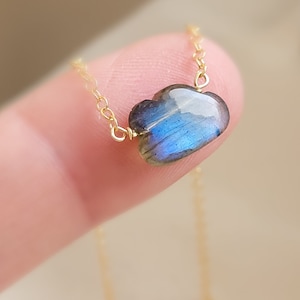 May include: A gold chain necklace with a heart-shaped labradorite gemstone pendant. The gemstone is a deep blue with iridescent flashes of color.