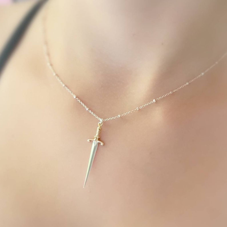 May include: A silver chain necklace with a small silver and gold sword pendant.