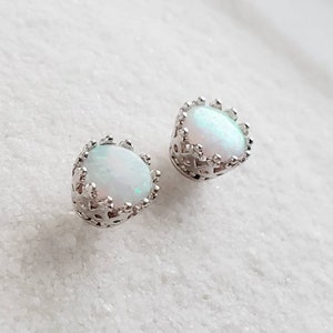 May include: A pair of silver earrings with white opal stones set in a crown-shaped design.