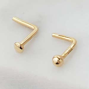 May include: Two gold nose rings with a small ball at the end. The rings are bent at a 90-degree angle.