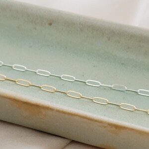 Dainty paperclip link chain necklace shown in 14k gold fill, and Sterling silver shown on a light green oblong ceramic dish. By Studio Blue on Etsy
