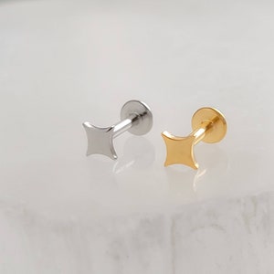 May include: Two small, flat, star-shaped studs, one silver and one gold, with a post and a flat back. The studs are on a white surface.
