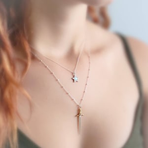May include: Two silver necklaces with a star and sword pendant. The star pendant is white and the sword pendant is gold.