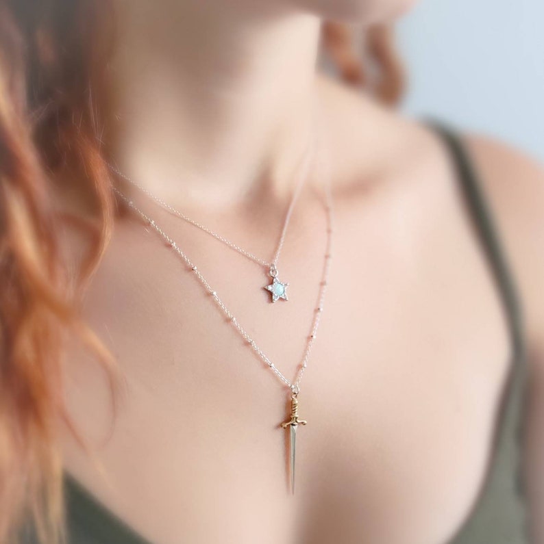 May include: Two silver necklaces with a star and sword pendant. The star pendant is white and the sword pendant is gold.