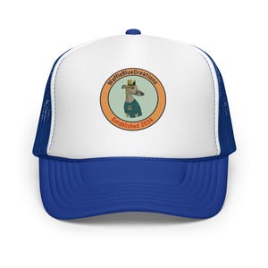 May include: A blue and white trucker hat. The front panel is white, with a blue brim and mesh back. The hat displays a circular logo with a dog wearing a hat and a shirt. The logo says "WaffleBlueCreations" and "Established 2024".