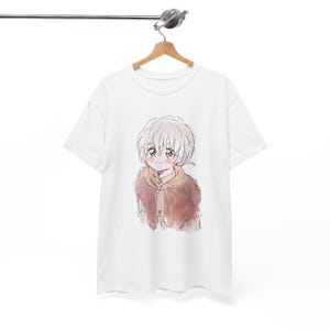 Könnte beinhalten: Weißes T-Shirt mit einer Aquarellillustration eines Anime-Charakters mit weißen Haaren und einem braunen, mit Fell gefütterten Mantel. Der Charakter hat rosige Wangen und einen sanften Ausdruck. Das T-Shirt hängt an einem Holzkleiderbügel.