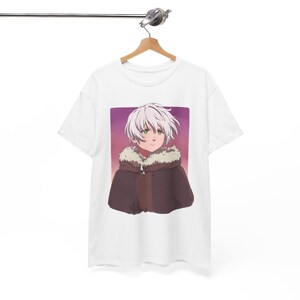 Könnte beinhalten: Weißes T-Shirt mit einer Cartoon-Illustration eines Charakters mit weißen Haaren, grünen Augen und einem braunen Umhang mit Pelzkragen. Das Kunstwerk ist vor einem lila-rosa Farbverlaufshintergrund platziert.