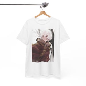 Könnte beinhalten: Weißes T-Shirt mit einer Anime-Illustration eines Charakters mit weißen Haaren und einem roten und braunen Umhang. Das Design ist vor dem Hintergrund eines winterlichen Waldes platziert. Das T-Shirt hängt an einem Holzbügel.