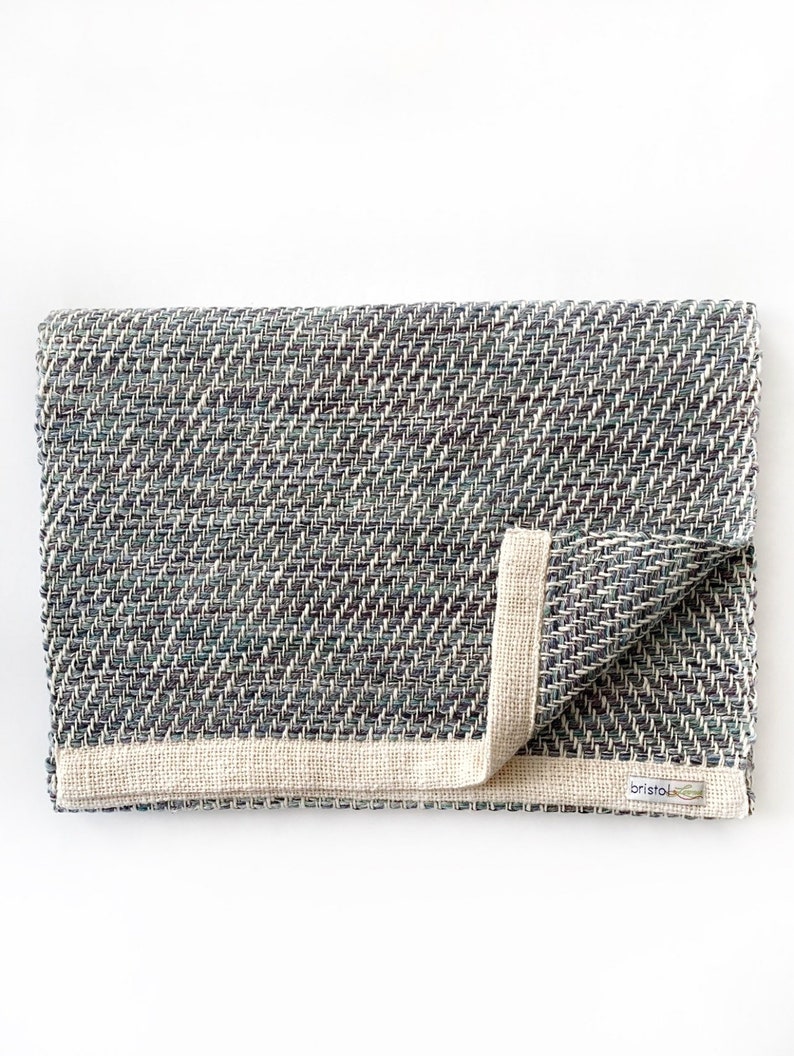 May include: A folded gray and white woven throw blanket with a cream colored border and a small "Bristol" label.