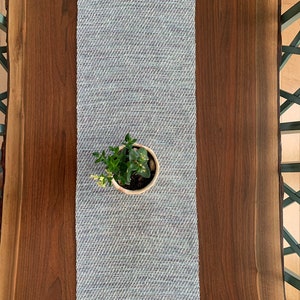 May include: A light blue woven table runner with a small potted plant in the center, on a dark brown wooden table.