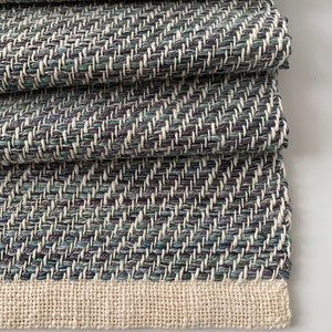 May include: A folded woven throw blanket with a chevron pattern in shades of blue, green, and white. The blanket has a cream-colored border.