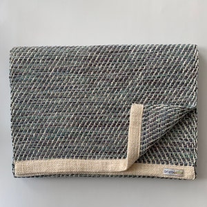 May include: A folded blue and white woven rug with a cream colored border and a "Bristol" label.